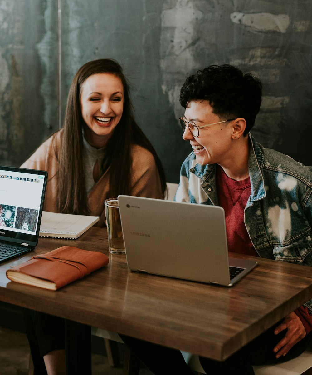 Dos compañeros de equipo trabajando con portátiles y sonriendo